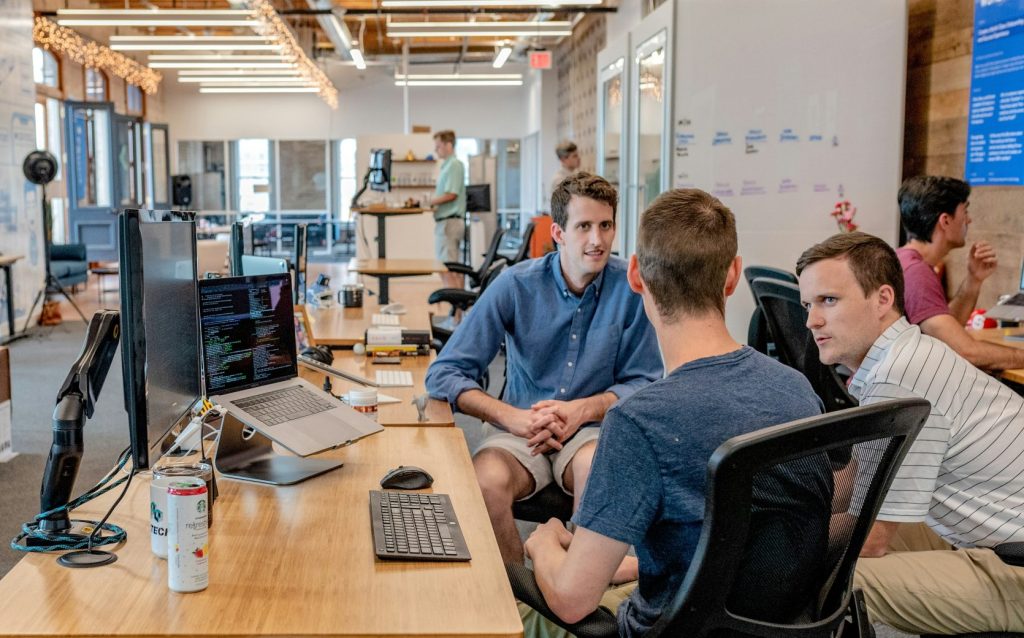 Drei Männer sitzen auf Stühlen neben Tischen