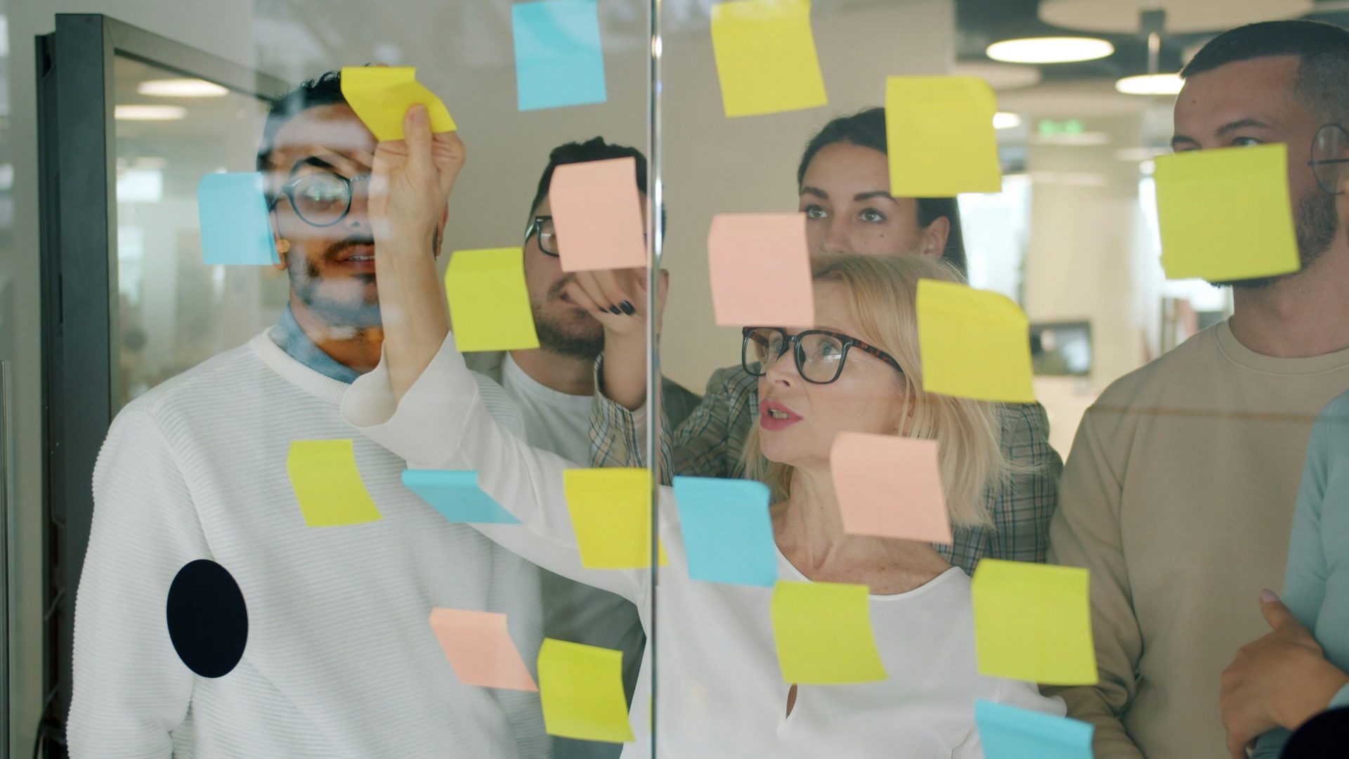 Séance de brainstorming en équipe avec des post-it sur une paroi vitrée.